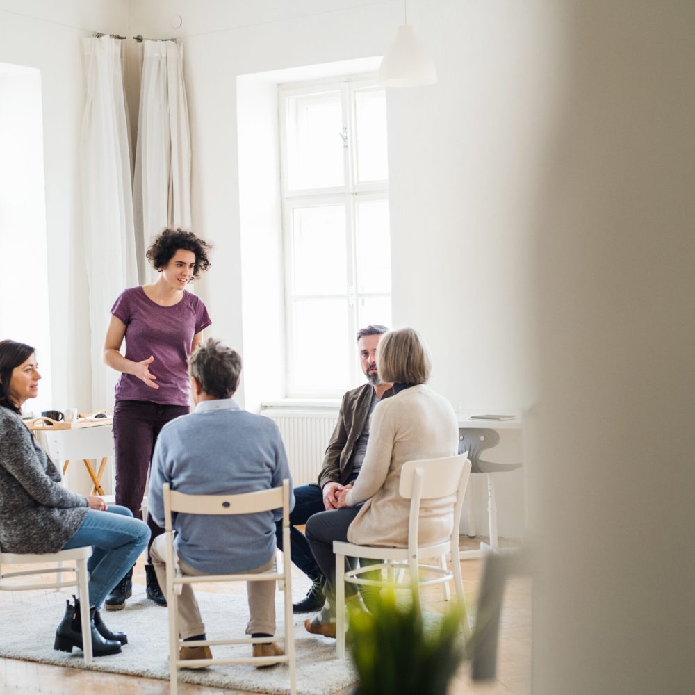 A young woman standing and talking to other people during group therapy.